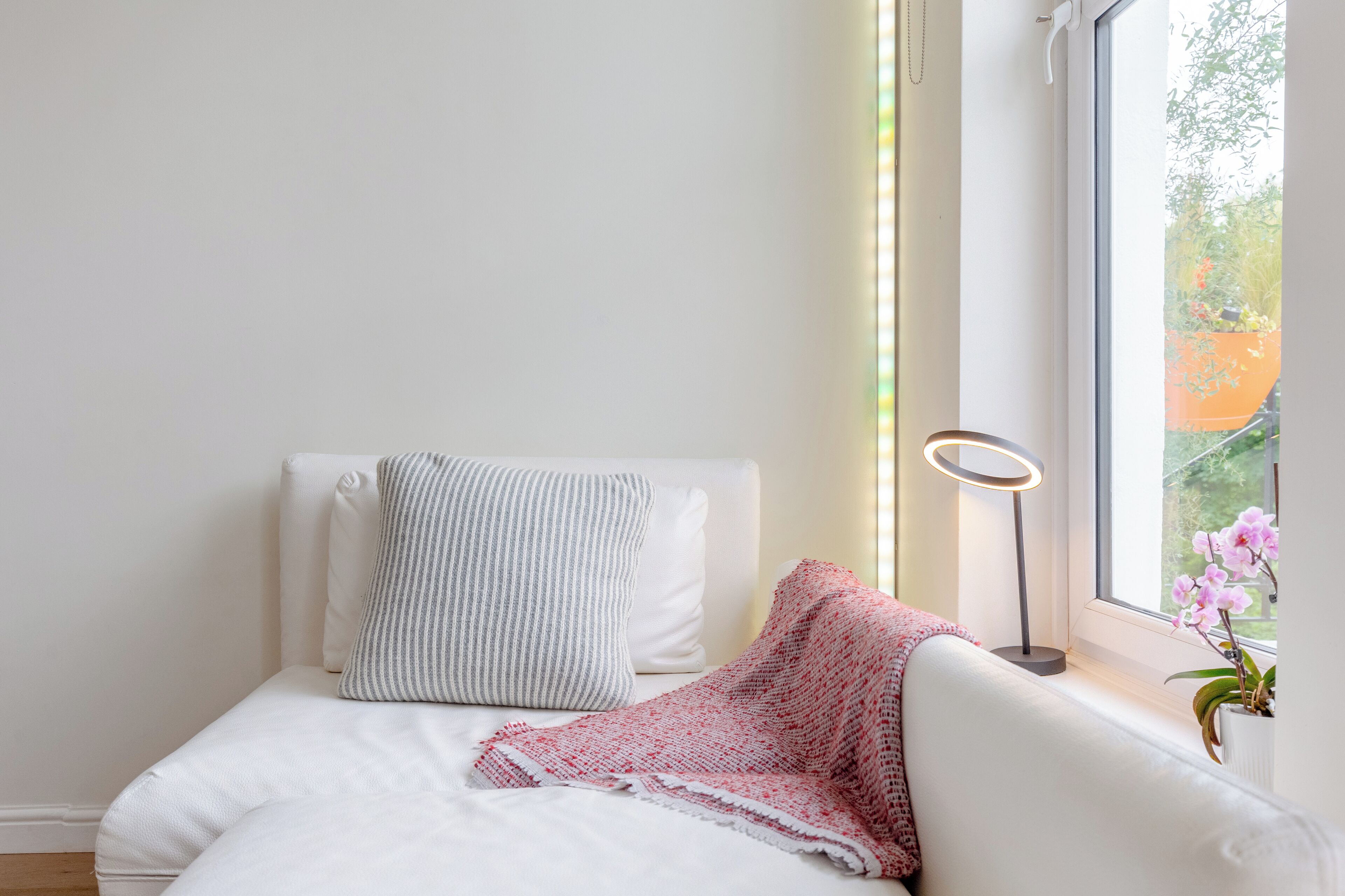 Une chambre à coucher bien rangée, avec un lit, des oreillers, une lampe de chevet et une fenêtre donnant sur un paysage verdoyant.