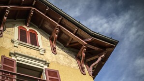 A corner of a building with a yellow facade, wooden beams, and red shutters.