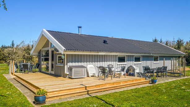 En enplansbyggnad med ett sluttande tak, en veranda och utomhusmöbler.