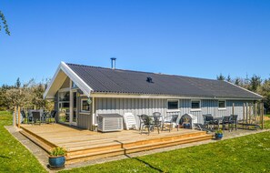 Ein eingeschossiges Gebäude mit Satteldach, einer Terrasse und Sitzgelegenheiten im Freien.