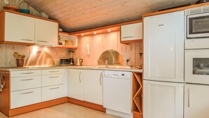 Ett kompakt kök med vita skåp, diskmaskin, kylskåp och detaljer i trä.