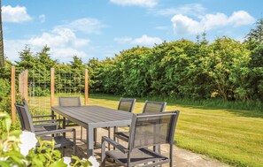 An outdoor patio with a table and chairs, surrounded by a metal fence and lush greenery. - Nice home in Løkken with kitchen (Løkken)