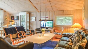 Ett mysigt vardagsrum med en tv, träpanel på väggarna och en matplats med stolar och ett bord.