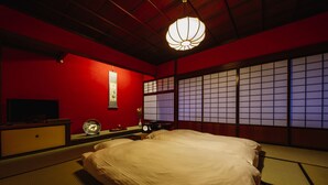 A traditional Japanese-style room with tatami flooring, a low bed, a desk with a lamp, and shoji screens. - asanogawa (Kanazawa)
