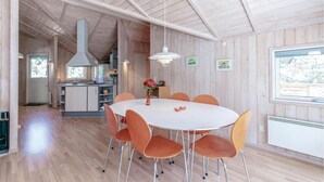 A modern kitchen with a central island, a dining area with a round table and orange chairs, and a large window providing a view of the outdoors. - Gorgeous home in Aakirkeby (Aakirkeby)