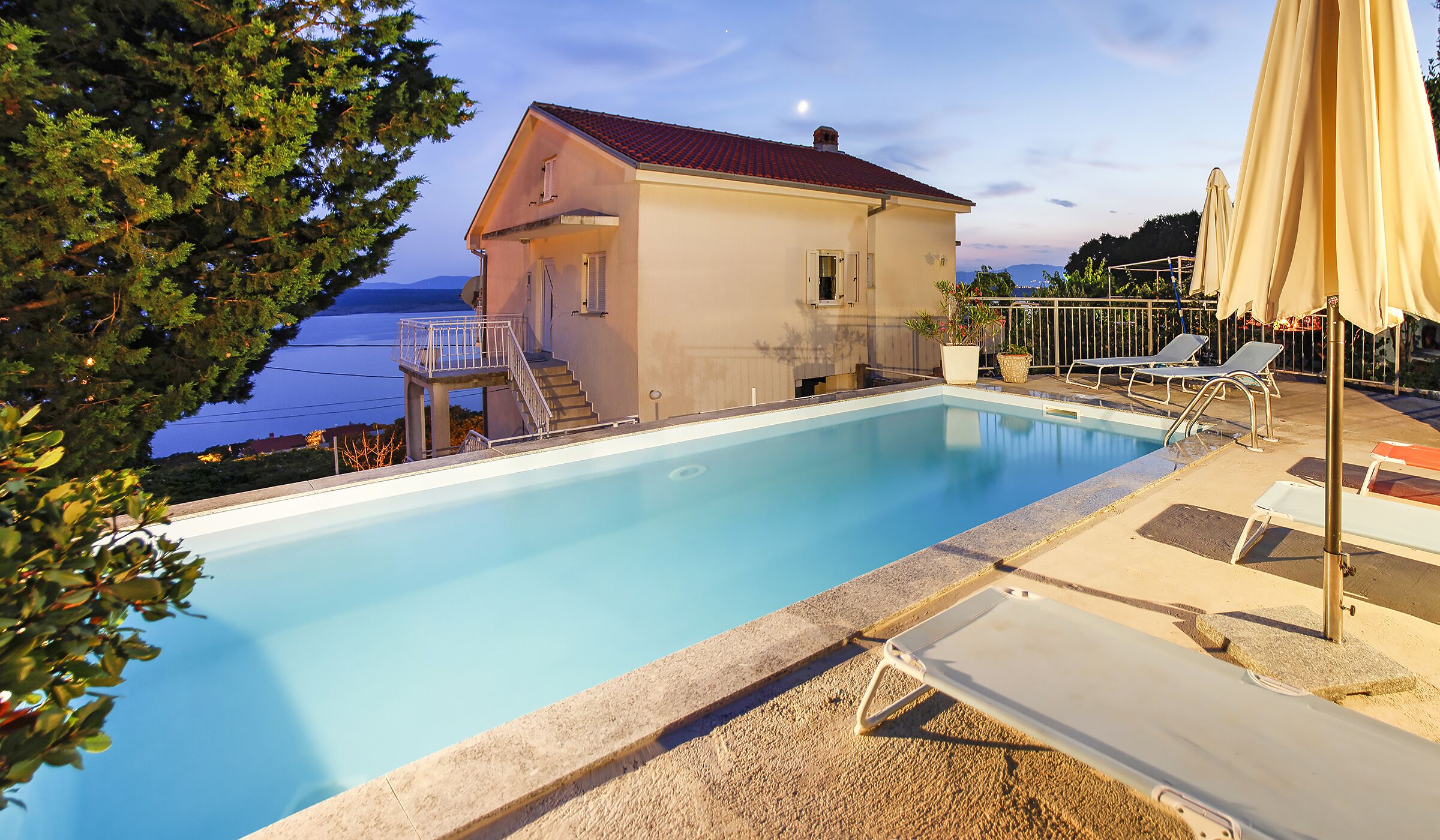 Ein Pool mit Meerblick, ein Haus mit Balkon und Liegestühle.