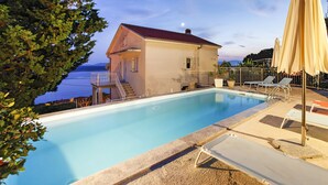 Une piscine avec vue sur la mer, une maison avec un balcon et des chaises longues.