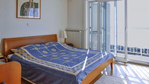 Une chambre à coucher comprenant un lit, une table de chevet, une lampe, un radiateur et une porte-fenêtre coulissante donnant sur un balcon.
