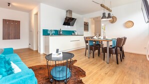 Un espace de vie moderne comprenant une cuisine, un coin repas et un coin salon confortable avec un canapé bleu et une table ronde.