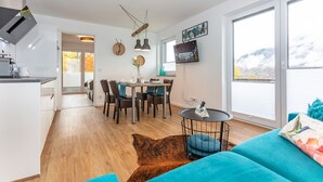 Une cuisine moderne avec des meubles blancs, un coin repas doté d’une table et de chaises en bois, et une grande fenêtre offrant une vue sur les montagnes.