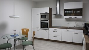 Een moderne keuken met witte kastjes, een ingebouwde magnetron, oven en een rvs-afzuigkap. Er staat een eettafel met stoelen en er hangt een hanglamp erboven.
