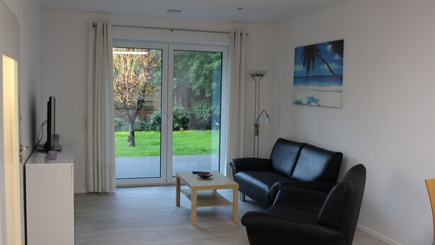 Een moderne woonkamer met een zwarte leren bank, een klein houten tafeltje en een witte koelkast.
