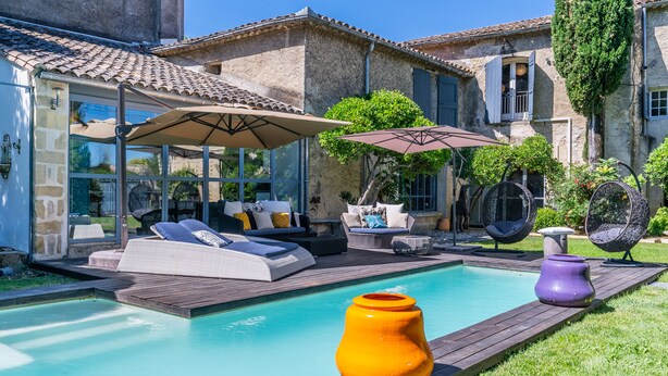 Ein Poolbereich mit Holzterrasse, Liegestühlen und Sonnenschirmen.