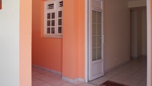 Un pasillo con una puerta blanca, una ventana, paredes anaranjadas y un suelo de baldosas.
