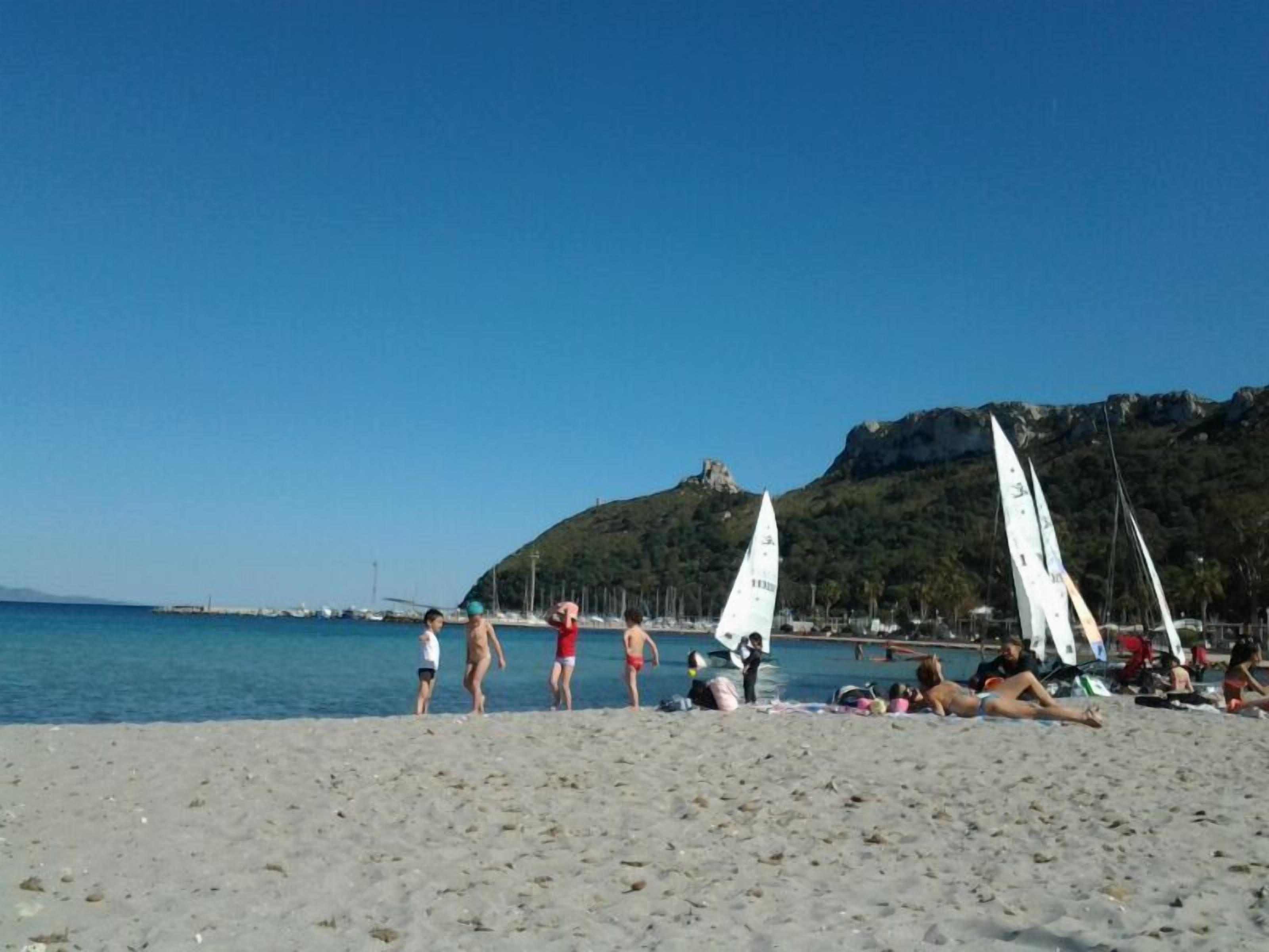 A beach with people, a sailboat, and a mountain in the background.