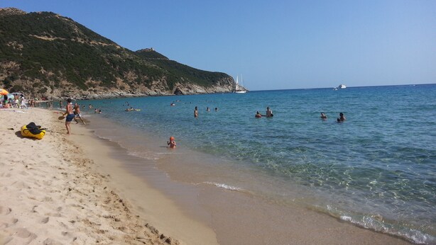 Ein Strand mit klarem Wasser, Menschen beim Schwimmen und Sonnenbaden, und ein Boot in der Ferne.