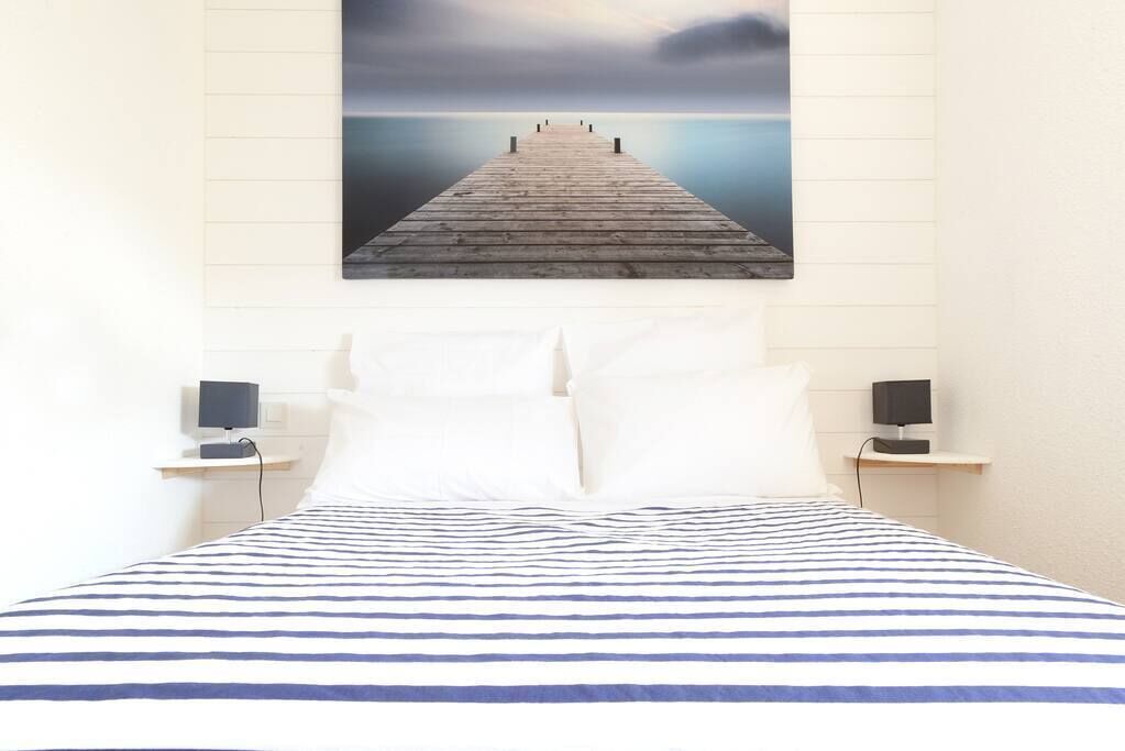 A bed with a striped bedspread, two white pillows, and two bedside tables with speakers.