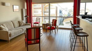 A modern living room with a sofa, a dining table with chairs, and a balcony with a view of buildings. - Arcachon - Élégant T3 de standing à proximité du centre-ville et plage (ARCACHON)