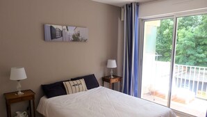 A bedroom with a large bed, two bedside tables, a painting on the wall, and a balcony with curtains. - Arcachon - Élégant T3 de standing à proximité du centre-ville et plage (ARCACHON)