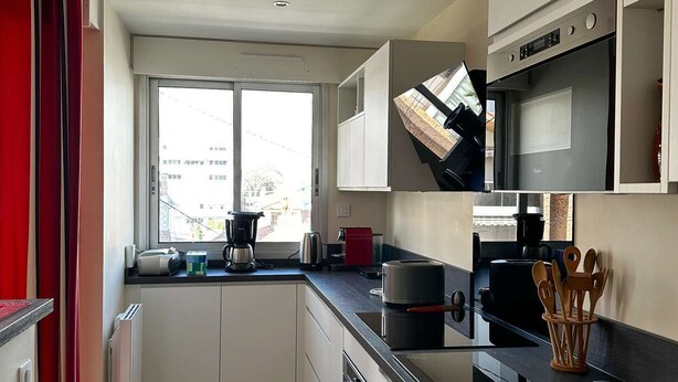 A compact kitchen with white cabinets, a black countertop, and a patterned floor. - Arcachon - Élégant T3 de standing à proximité du centre-ville et plage (ARCACHON)