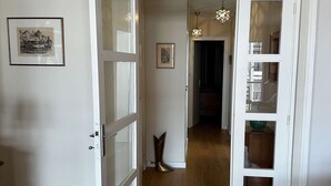 A hallway with wooden flooring, white walls, and a door leading to a room with a green bowl on a wooden cabinet. - Arcachon - Élégant T3 de standing à proximité du centre-ville et plage (ARCACHON)