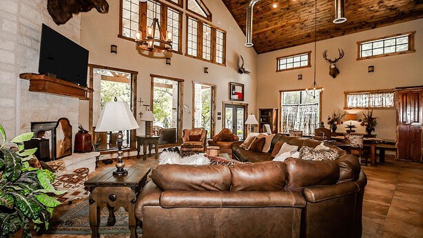 A spacious living room with a large brown leather sofa, wooden ceiling, and mounted animal heads.