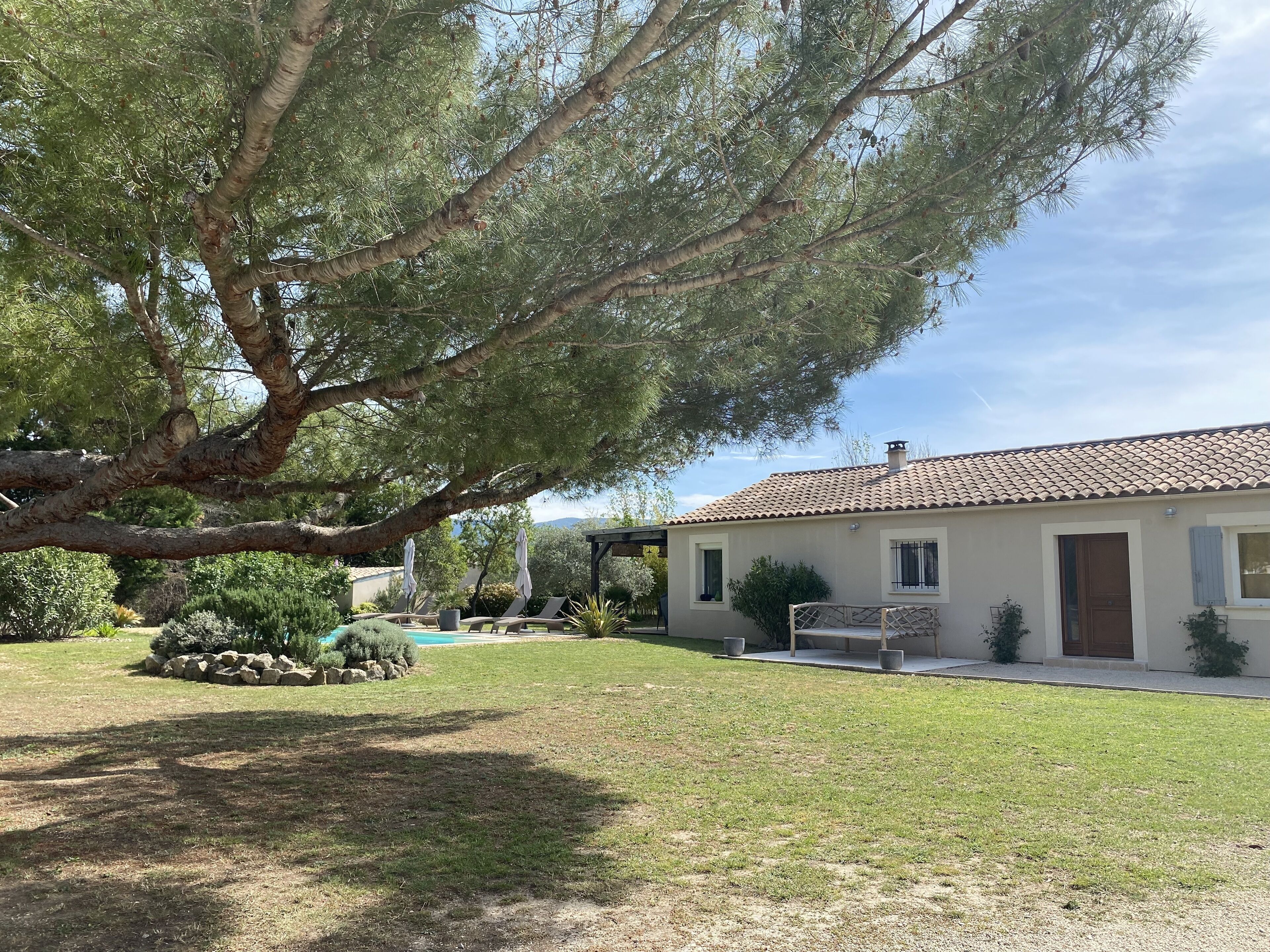 Une maison avec un toit en tuiles, une pelouse et un grand arbre.