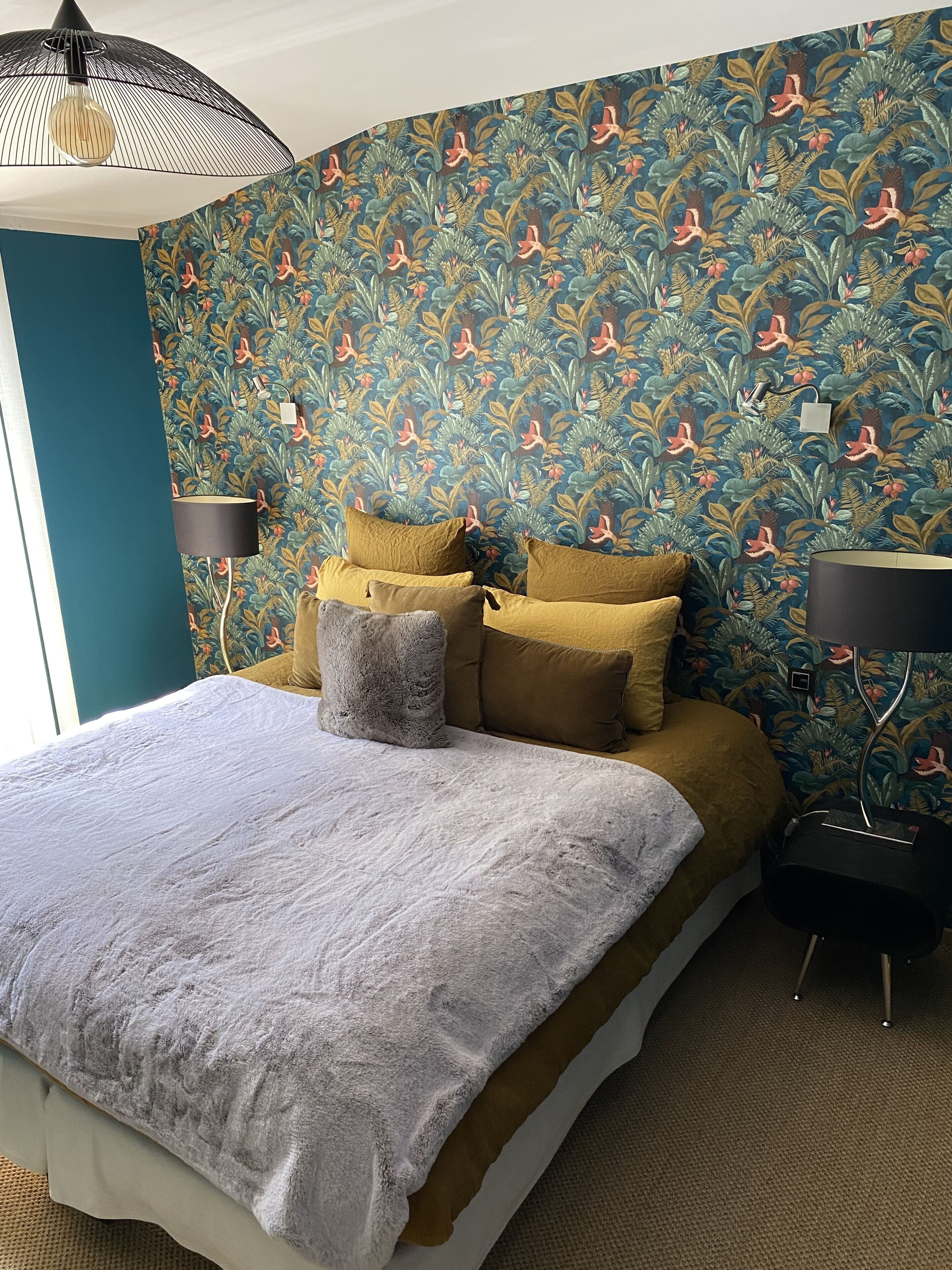 A bedroom with a large bed, two bedside lamps, and a patterned wallpaper.