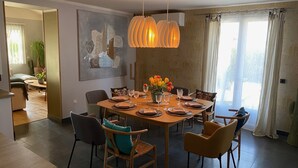 Un comedor con una mesa redonda dispuesta para seis personas, rodeada de sillas con cojines. Encima de la mesa, una lámpara colgante moderna, y en la pared, un cuadro abstracto de gran tamaño.