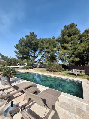 Une piscine entourée d’arbres et d’une clôture, avec des chaises longues et un hamac à proximité.