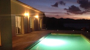 Piscina com deck de madeira e um edifício com várias portas e luzes.