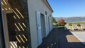 Um deck de madeira com parede de pedra e venezianas, com vista para uma piscina e montanhas.