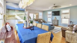 Un salon spacieux avec une grande table bleue, des sièges confortables et un grand tableau accroché au mur.