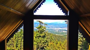 Ein Zimmer mit einer dreieckigen Holzzahlendecke und einem großen Fenster mit Blick auf einen Wald und Berge.