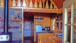Ein gemütliches Blockhauss-Interieur mit Kamin aus Stein, einem Holzespeisesaal und einer Küchenzeile mit Mikrowelle und Kühlschrank.