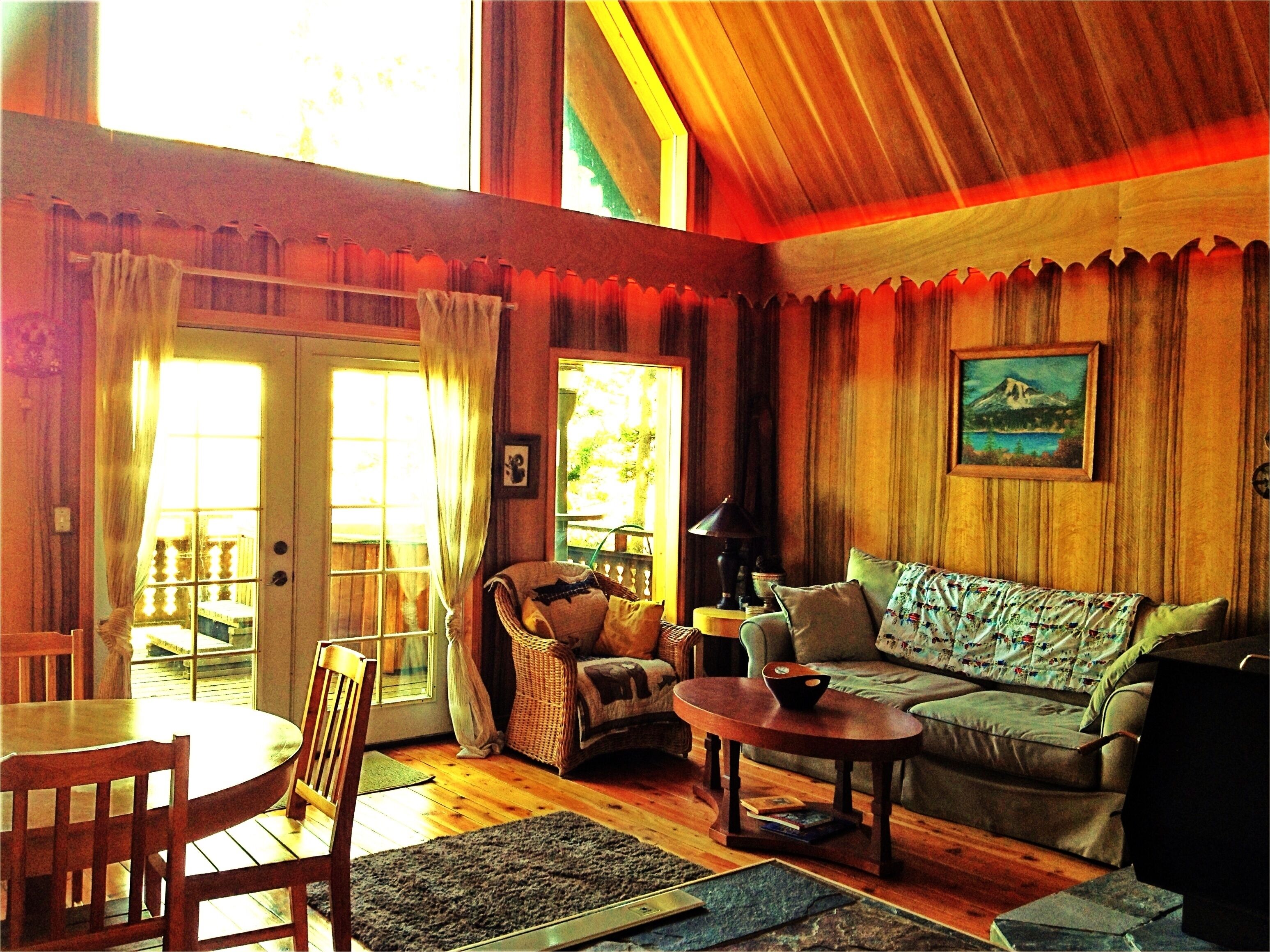 A cozy living room with a wooden floor, a sofa, a chair, a table, and a painting on the wall.