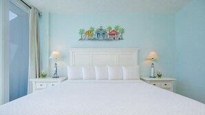 A hotel room with a large bed, two bedside tables, a headboard, and a wall-mounted artwork of colorful houses. - LIGHTHOUSE! Popular Property! ~ 1 BR Beach Front! XTRA BATH! (Gulf Shores)