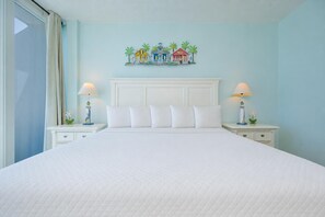 Hotelkamer met een groot bed, twee nachtkastjes, een hoofdbord en een wanddecoratie van kleurrijke huizen.