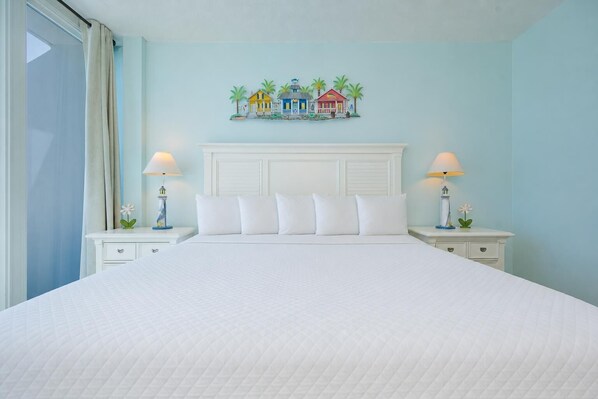 Une chambre d’hôtel avec un grand lit, deux tables de chevet, une tête de lit et une œuvre d’art colorée représentant des maisons, accrochée au mur.