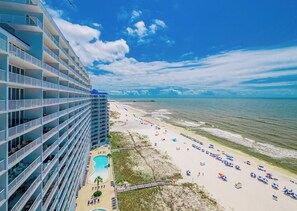 Un hôtel de grande hauteur doté de nombreux balcons, offrant une vue sur une plage parsemée de parasols et sur une piscine.