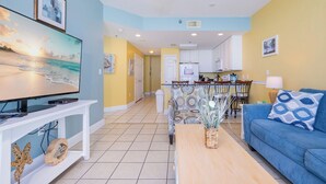 A living room with a TV, sofa, and coffee table, a kitchen with white cabinets, and a dining area with chairs. - LIGHTHOUSE! Popular Property! ~ 1 BR Beach Front! XTRA BATH! (Gulf Shores)