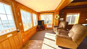 A cabin with wooden walls, large windows, a television, a fireplace, and a cozy seating area. - Lakeside Cabin on Lake Noquebay - Including Your Own Pier, Kayak/Canoes, & More! (Crivitz)