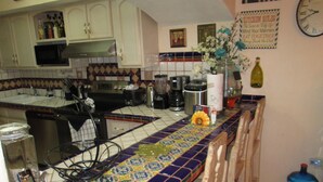 A kitchen with white cabinets, a microwave, a toaster, and a coffee maker. There is a clock on the wall and a sign with kitchen rules.