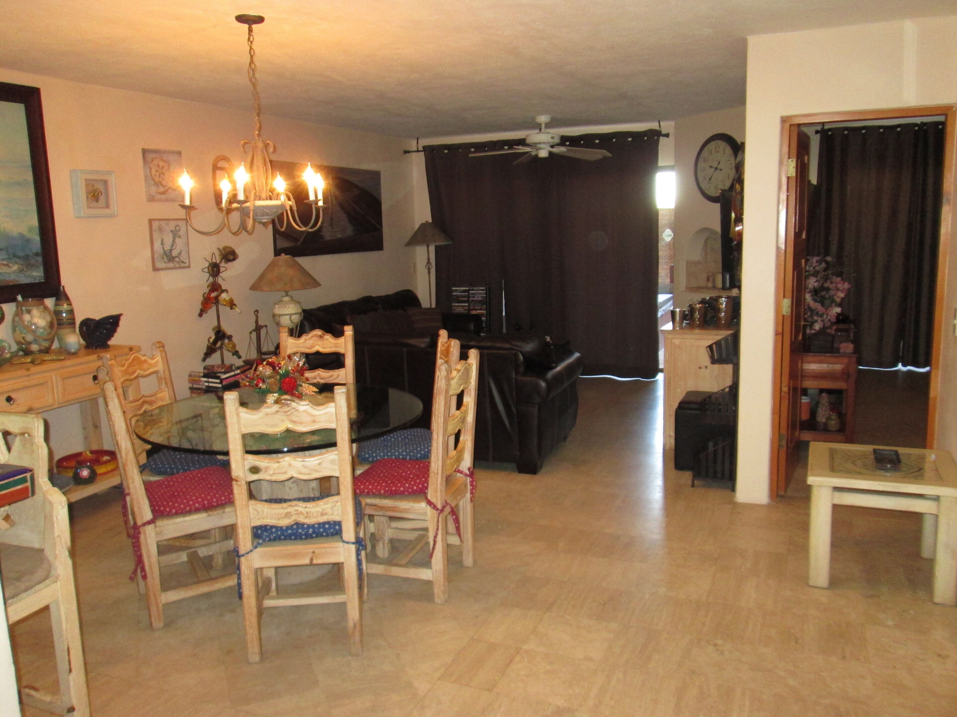 Un salon comprenant une table à manger, des chaises, un lustre, un canapé, un téléviseur et une horloge murale.