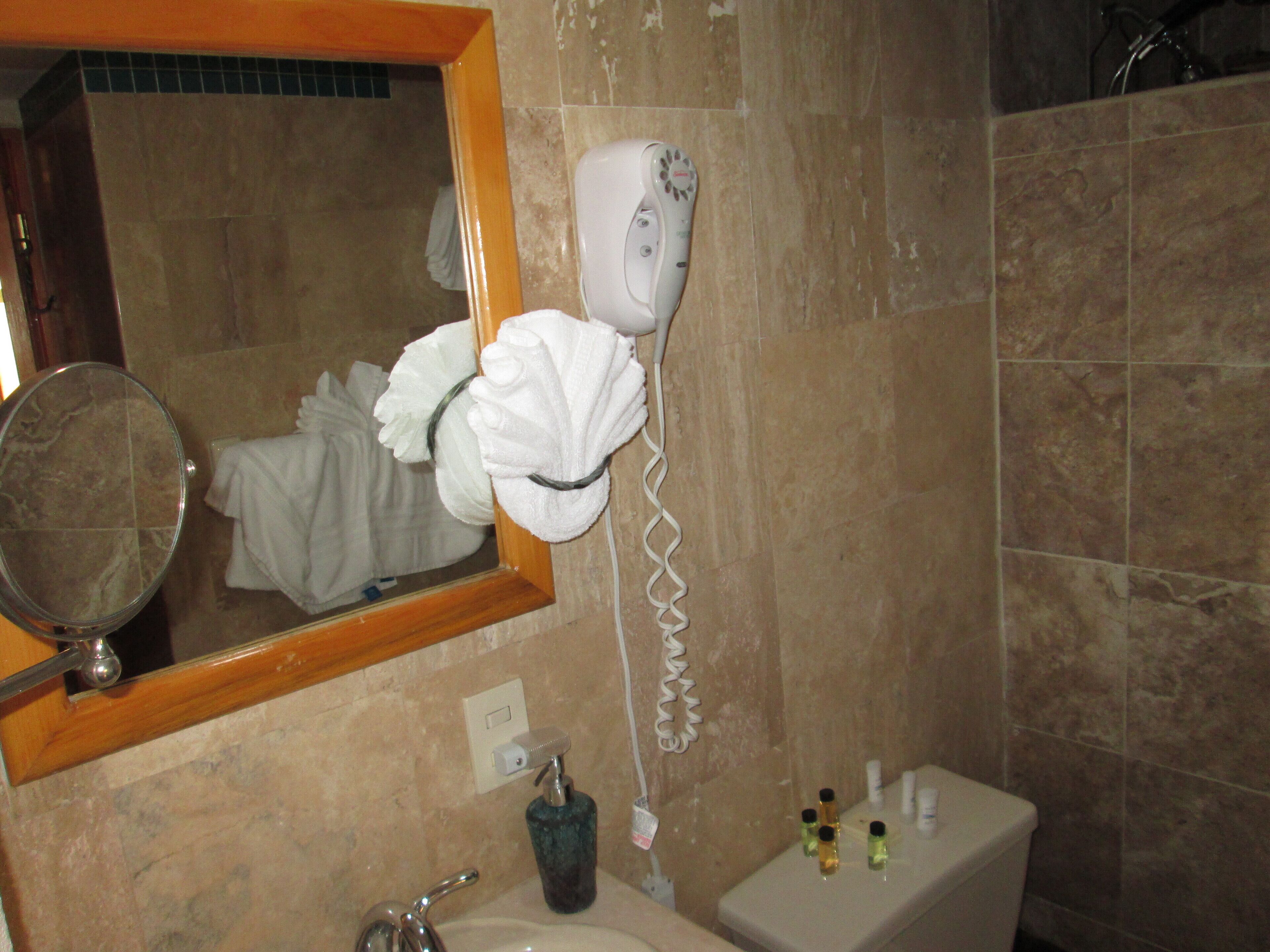 Een badkamer met een föhn aan de muur, een wastafel, een spiegel en toiletartikelen op het aanrecht.