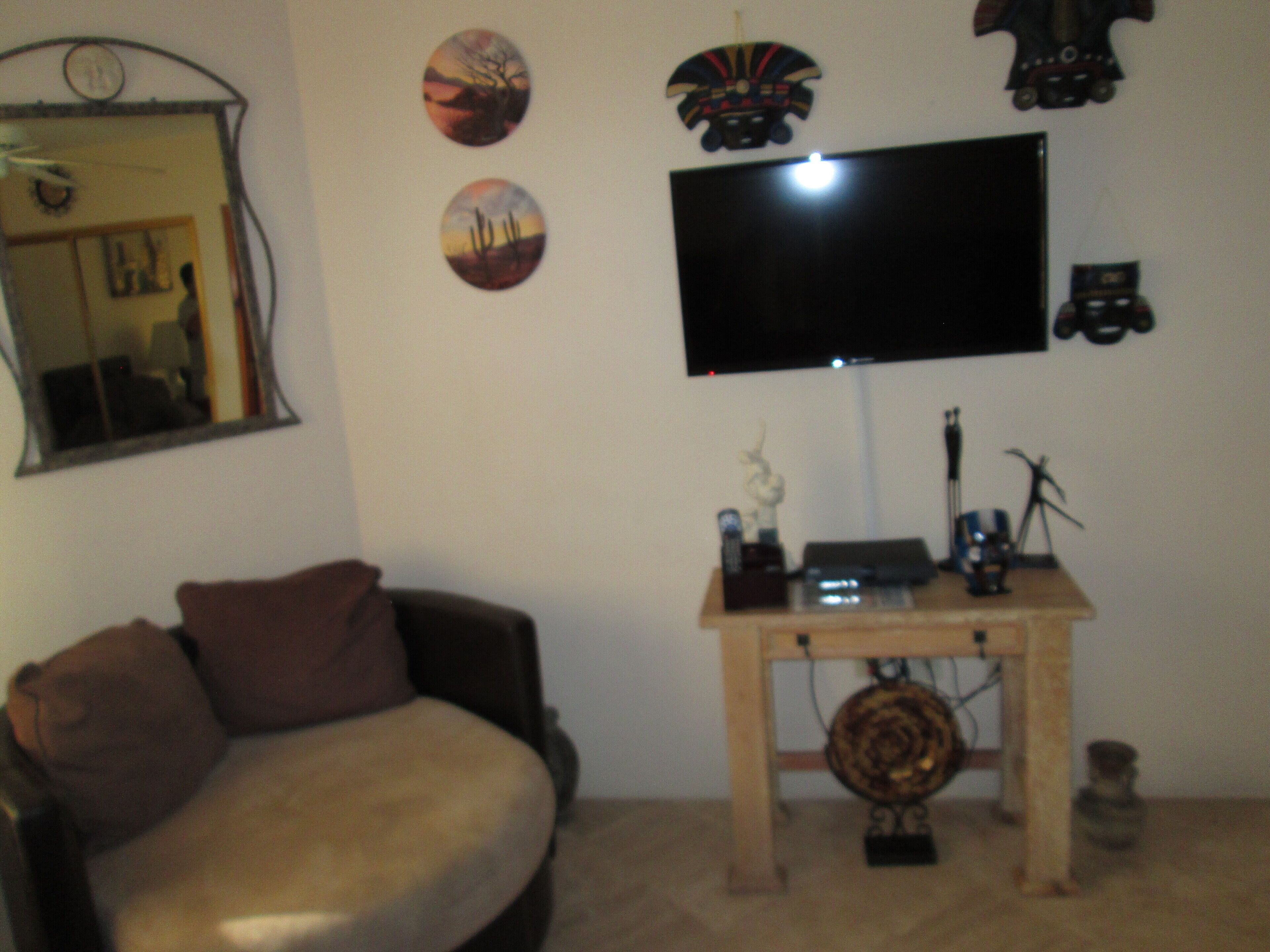A living room with a sofa, a flat-screen TV mounted on the wall, and a small wooden table with decorative items.