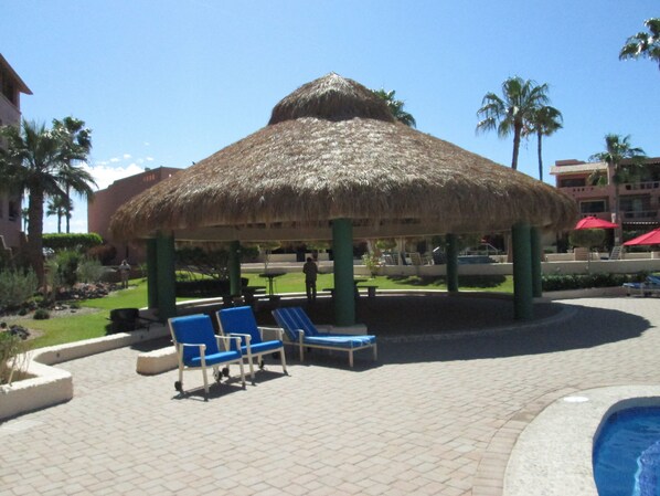 Un pabellón con techo de paja, sillones azules y zona de piscina.
