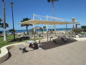 An outdoor seating area with stone tables and benches, a pergola structure, and a view of the ocean.