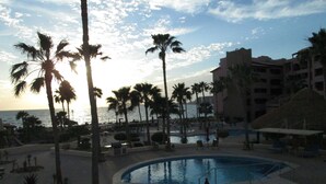 A resort pool area with palm trees, a pool, and a view of the ocean.