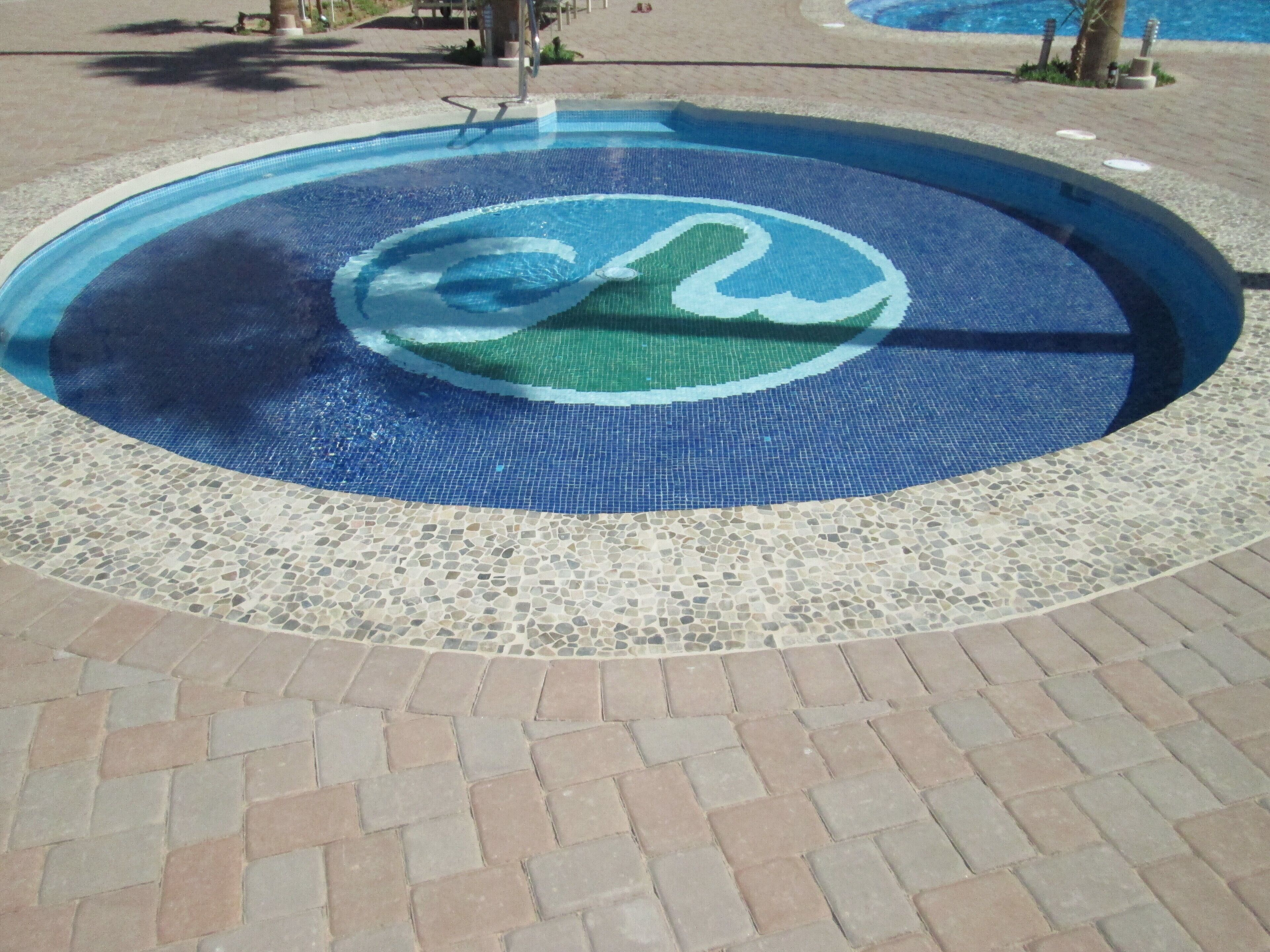 Une piscine circulaire ornée d’une mosaïque et entourée d’une allée dallée.